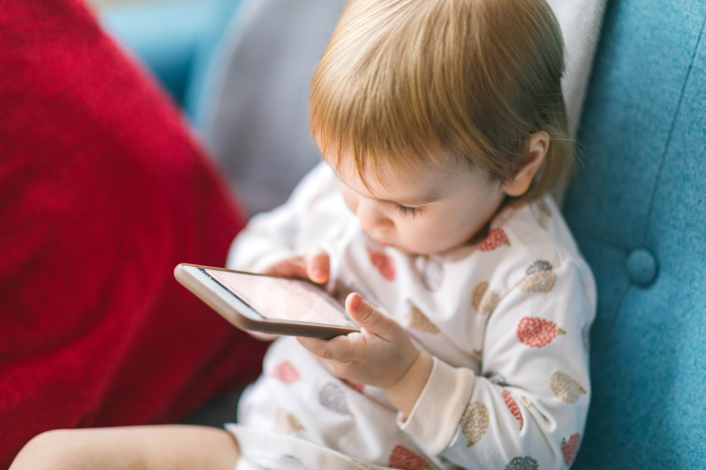Criança, sentada, olha para a tela de um smartphone que está em suas mãos