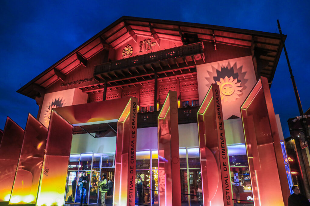 Crédito: Edison Vara/Agência Pressphoto. [Descrição da imagem: A foto mostra, ao fundo, um prédio baixo de madeira e, à frente, uma estrutura de vidro. Luzes vermelhas iluminam o local.]