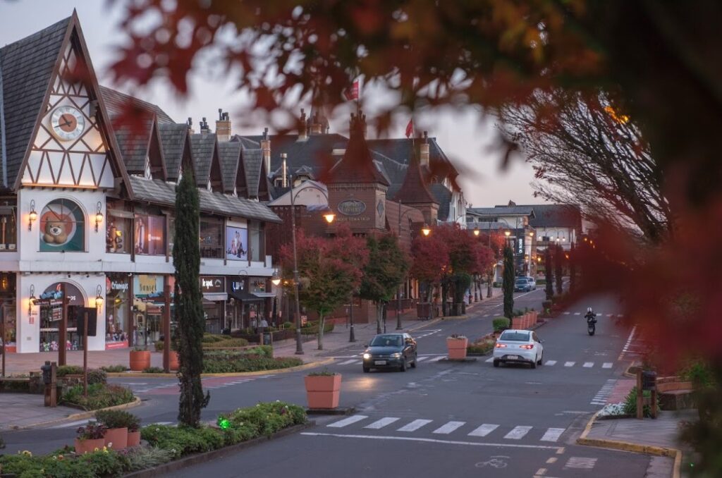 Crédito: Rafael Cavalli. [Descrição da imagem: A foto mostra uma rua com dois carros e uma moto indo para lados opostos. Há prédios baixos em estilo alemão e plantas verdes nos canteiros centrais da rua e laterais das calçadas. Uma árvore está próxima a câmera, desfocada.]