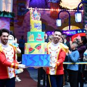 Dois meninos do artístico, uniformizados, seguram o bolo temático da Vila da Mônica com confetes e dizeres "1 ano da Vila"